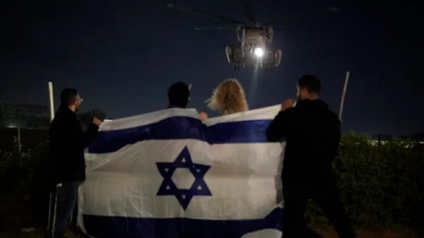 Gente sosteniendo una bandera israelí mira la llegada de un helicóptero que transporta a rehenes israelíes liberados por Hamas en el Centro Médico Sheba en Ramat Gan, Israel (AP Foto/Leo Correa)